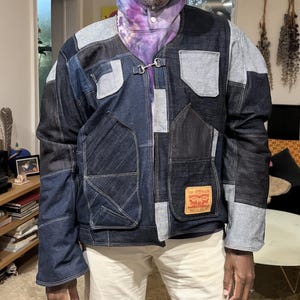 May include: A patchwork denim jacket in shades of blue and grey, with a metal clasp and two front pockets. The Levi Strauss & Co. label is visible. The person is wearing a tie-dye hoodie. The jacket is made of various denim panels.