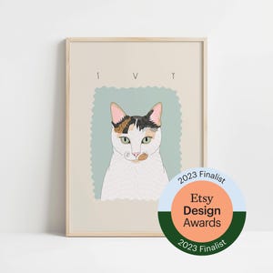Könnte beinhalten: Ein gerahmter Kunstdruck mit einem Katzenporträt und dem Namen "IVY" darüber. Die Katze hat weißes Fell mit schwarzen, braunen und orangefarbenen Flecken. Der Druck ist in einem hellen Holzrahmen und enthält einen "Etsy Design Awards 2023 Finalist" Aufkleber.