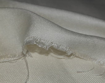 May include: Close-up of a white fabric with a textured weave. The fabric has a frayed edge.