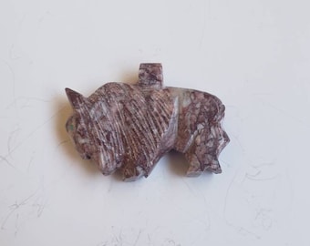 May include: A carved stone bison pendant with brown, white, and gray marbling. The pendant has a loop at the top for attaching to a chain or cord.