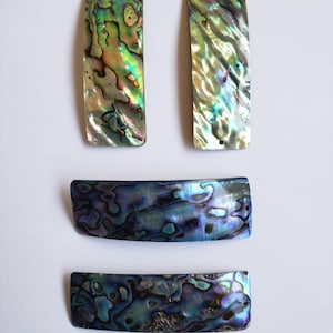 May include: Four iridescent abalone shell hair clips. Two are long and narrow, and two are shorter and wider. The shells have a variety of colours, including green, blue, purple, and gold.