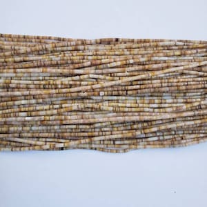 Puede incluir: Una hebra de cuentas de concha marrón y blanca. Las cuentas son largas y delgadas, y tienen un aspecto natural y orgánico.