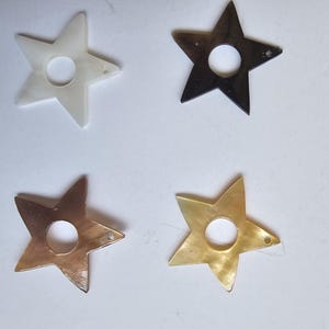 May include: Four star-shaped ornaments with a circular cutout in the center. The set includes one white, one dark brown, one light brown, and one golden-yellow star, each featuring a small hole near one point for hanging or attachment purposes.
