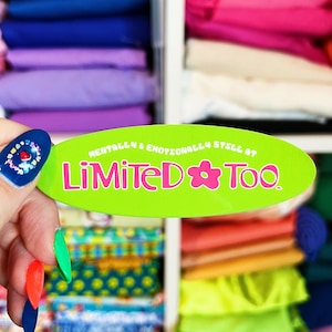 May include: A green oval sticker with the text "Mentally & Emotionally Still At Limited Too" in pink and white lettering. A pink flower with a white center is between the words "Limited" and "Too".