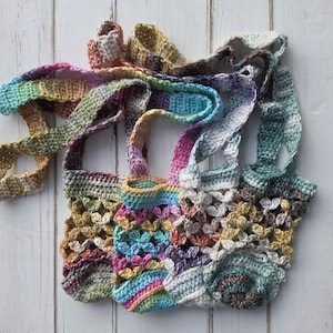 May include: A collection of three small, handmade crochet bags featuring a variegated yarn pattern in shades of pink, blue, yellow, green, and purple. Each bag has an openwork floral stitch design, a solid base, and a long, integrated shoulder strap.