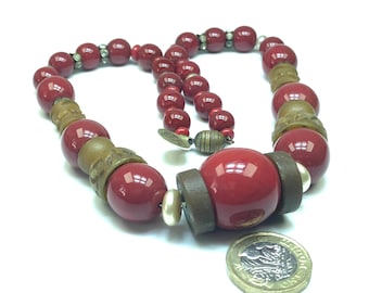 Pode incluir: Um colar de contas vermelhas e marrons com uma grande conta vermelha no centro. O colar é feito de vários materiais, incluindo madeira, vidro e metal.
