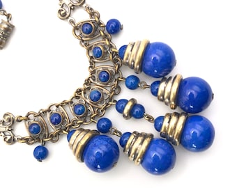 May include: A gold and blue statement necklace with a chain design and multiple dangling blue beads.