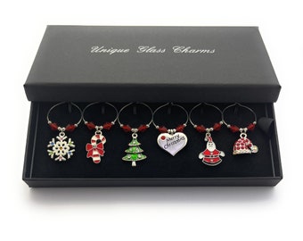 May include: Set of six silver-tone Christmas-themed wine glass charms with red crystal accents. The charms feature a snowflake, candy cane, Christmas tree, heart with "Merry Christmas" text, Santa Claus, and a Santa hat.