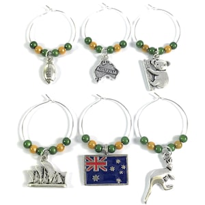 May include: Set of six Australian themed wine glass charms. Each charm features a different Australian icon, including a koala, kangaroo, rugby ball, the Sydney Opera House, the Australian flag, and a map of Australia. The charms are made of silver metal and have green and gold beads.