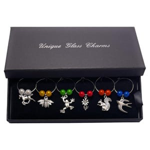 May include: Set of six glass charms in a black box. Each charm features a different animal or insect, including a horse, bee, frog, flower, squirrel, and bird. The charms are silver with colourful beads.