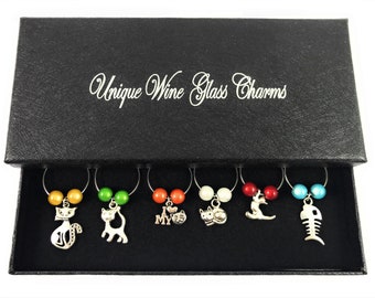 May include: Set of six wine glass charms in a black box. Each charm features a different cat-themed design, including a cat, a fishbone, and a heart with the words "I love my cat".