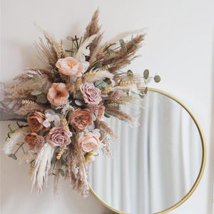 May include: A gold round mirror with a bouquet of dried pampas grass and blush pink flowers.