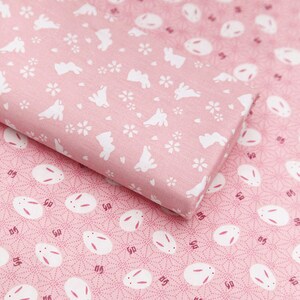 Op de afbeelding: Twee roze stofstalen met een herhalend patroon van witte konijnen. De bovenste staal heeft een eenvoudige konijnen-silhouet met kleine witte bloemen. De onderste staal heeft een gedetailleerdere konijnen-silhouet met een cirkelpatroon.