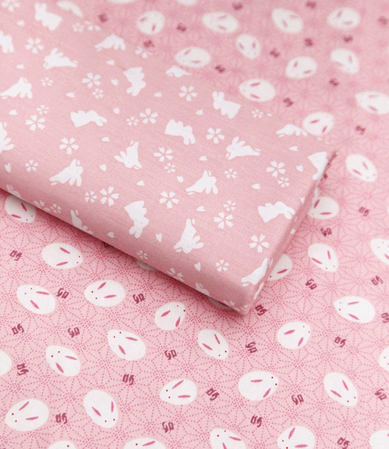 Op de afbeelding: Twee roze stofstalen met een herhalend patroon van witte konijnen. De bovenste staal heeft een eenvoudige konijnen-silhouet met kleine witte bloemen. De onderste staal heeft een gedetailleerdere konijnen-silhouet met een cirkelpatroon.