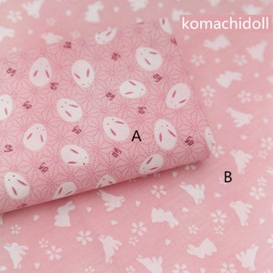 Op de afbeelding: Twee roze stofstalen met witte konijnenpatronen. De bovenste staal heeft een herhalend patroon van konijnen met een klein wit stippenpatroon. De onderste staal heeft een herhalend patroon van konijnen met een klein wit bloemenpatroon. De tekst "komachidoll" is afgedrukt in de rechterbovenhoek van de afbeelding.