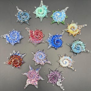May include: A collection of twelve colorful, star-shaped glass pendants. Each pendant features a spiral design in shades of blue, green, red, yellow, and purple. The pendants are clear with a glossy finish.