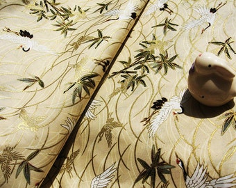 May include: A beige fabric with a repeating pattern of stylized cranes and bamboo branches. The fabric has a subtle gold sheen. A white ceramic figurine of a rabbit is placed on the fabric.