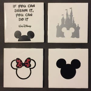 May include: Set of four white ceramic coasters with black and gray Mickey Mouse silhouettes. One coaster features the quote "If you can dream it, you can do it" with the Walt Disney logo. Another coaster features a gray silhouette of the Cinderella Castle.