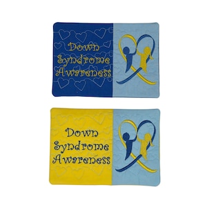 May include: Two rectangular fabric patches featuring embroidered Down Syndrome Awareness designs. One patch has a dark blue background with yellow text and a light blue side, while the other has a yellow background with dark blue text and a light blue side.