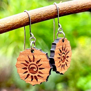 May include: A pair of wooden earrings with a sun design. The earrings are made of light brown wood and have a silver hook.