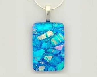 Könnte beinhalten: Eine rechteckige Halskette mit einem blauen, schillernden Glasanhänger. Der Anhänger hat ein mosaikartiges Muster mit weißen und blauen Akzenten.