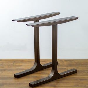 May include: Two metal table legs in a dark bronze finish. The legs are made of sturdy metal and have a simple, modern design.