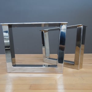 Pode incluir: Duas pernas de mesa de metal prateado com um design de moldura quadrada. As pernas são de metal polido e têm uma superfície reflexiva.