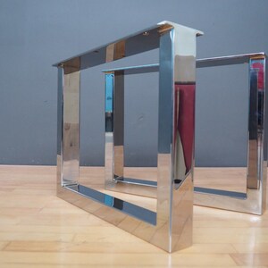 May include: Two polished chrome metal table legs with a square design. The legs are made of thick metal and have a shiny finish.