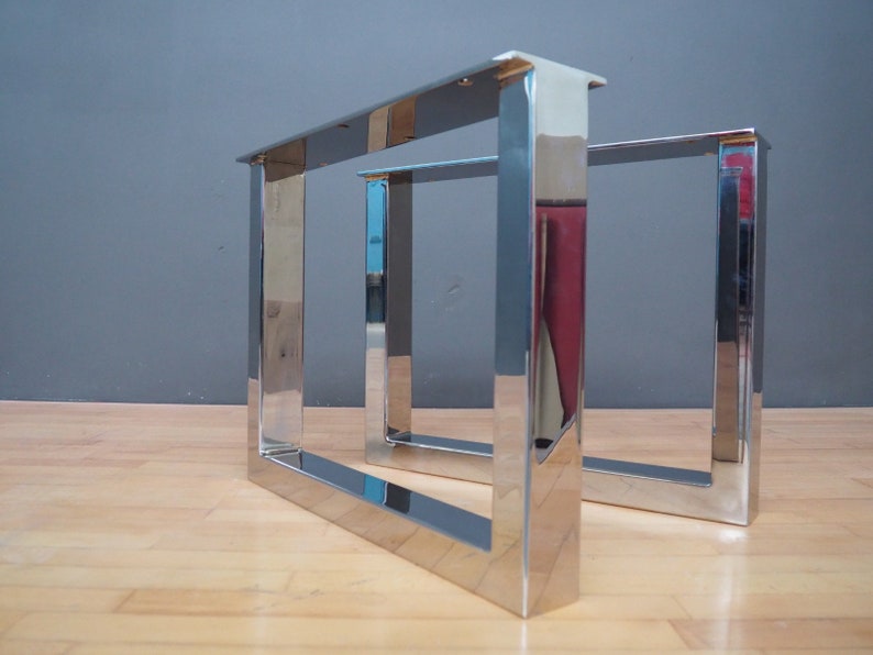 May include: Two polished chrome metal table legs with a square design. The legs are made of thick metal and have a shiny finish.