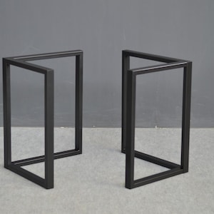May include: Two black metal table legs with a square base and a rectangular top. The legs are made of a sturdy metal and have a simple, modern design.