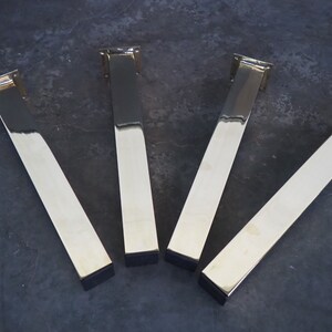 Four polished gold metal table legs with square bases