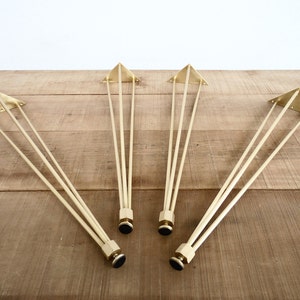 May include: Four gold metal hairpin legs with black feet. The legs are triangular in shape and have a sleek, modern design.