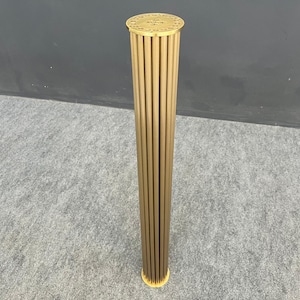 Peut inclure: Une colonne en métal doré avec un sommet décoratif et un motif cannelé. La colonne est posée sur un tapis gris.