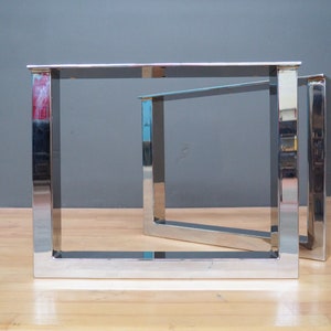 May include: Two silver metal table legs with a square frame design. The legs are made of polished metal and have a modern, industrial look.