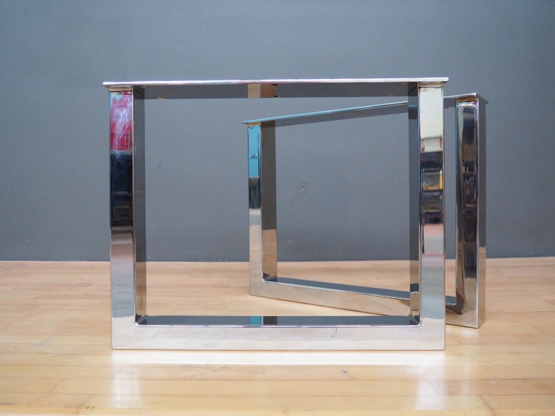 May include: Two silver metal table legs with a square frame design. The legs are made of polished metal and have a modern, industrial look.
