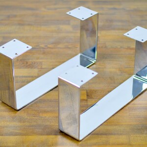 Pode incluir: Quatro pernas de mesa de metal cromado com um design em forma de U. As pernas são polidas e têm um acabamento brilhante.