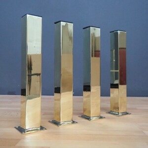 May include: Four polished gold metal table legs with square bases.