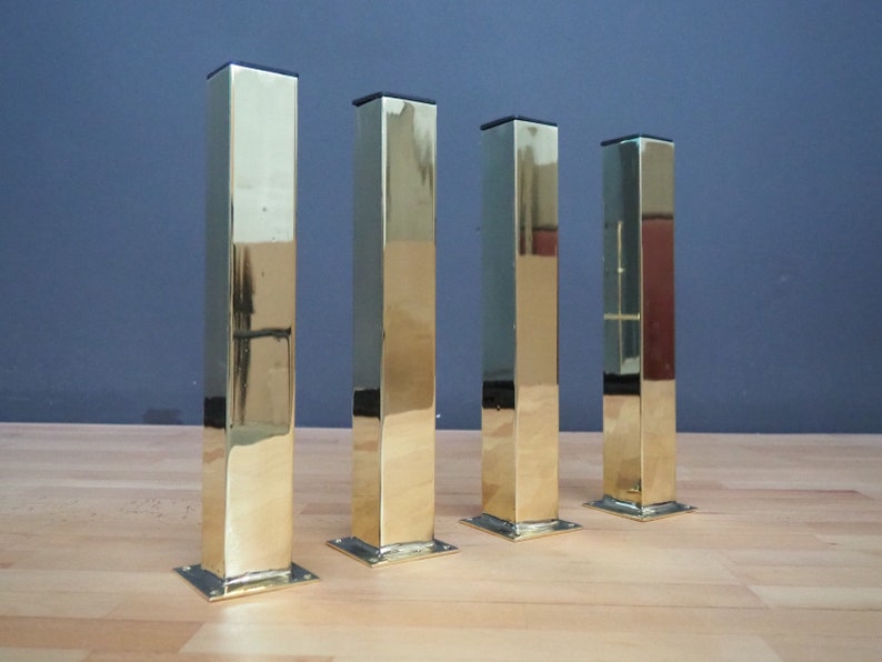 May include: Four polished gold metal table legs with square bases.