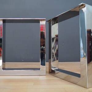 May include: Two polished chrome table legs with a square design. The legs are made of thick metal and have a shiny finish.