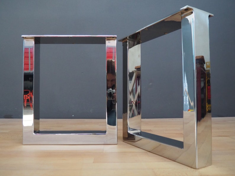 May include: Two polished chrome table legs with a square design. The legs are made of thick metal and have a shiny finish.
