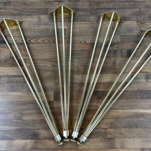 May include: Four sets of gold metal hairpin legs for furniture. Each leg has three prongs and a triangular base.