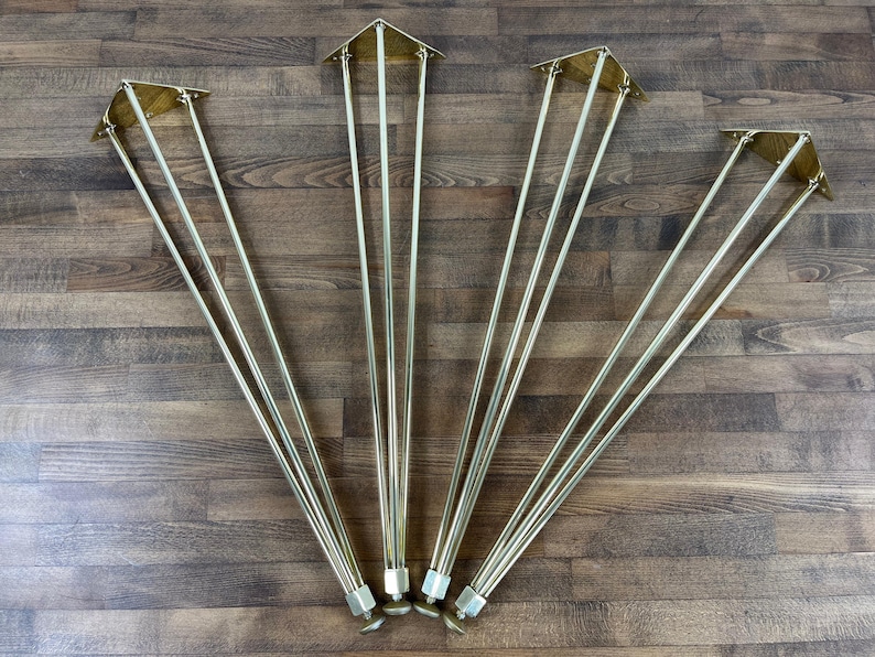 May include: Four sets of gold metal hairpin legs for furniture. Each leg has three prongs and a triangular base.