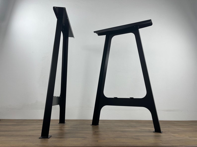 Two black metal table legs, each with a triangular shape and a flat top. The legs are standing on a wooden surface.