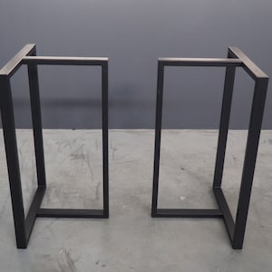 May include: Two black metal table legs with a square base and a rectangular top.