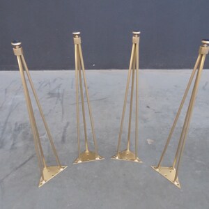 May include: Four gold metal hairpin legs for furniture. Each leg has a triangular base and a black rubber tip.