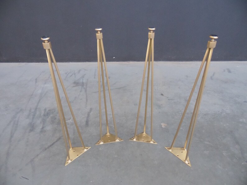 May include: Four gold metal hairpin legs for furniture. Each leg has a triangular base and a black rubber tip.