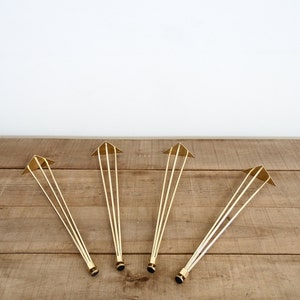 May include: Four gold metal hairpin legs for furniture. Each leg has a triangular base and three prongs.