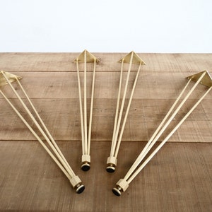 May include: Four gold metal hairpin legs for furniture. Each leg has a triangular base and three rods.