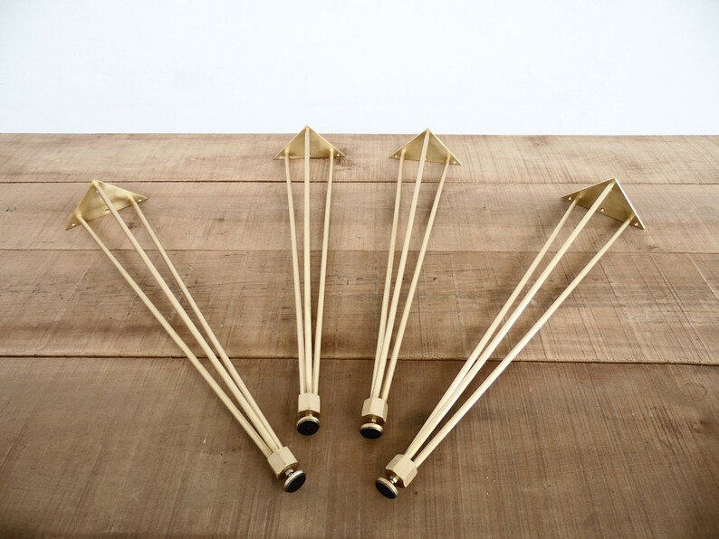 May include: Four gold metal hairpin legs for furniture. Each leg has a triangular base and three rods.