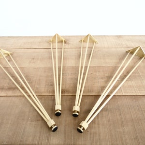 May include: Four gold metal hairpin legs for furniture. Each leg has a triangular base and three rods extending from the base.